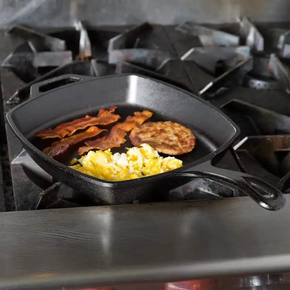 Square cast iron skillet frying pan with black handles cooking bacon and eggs on a gas stove