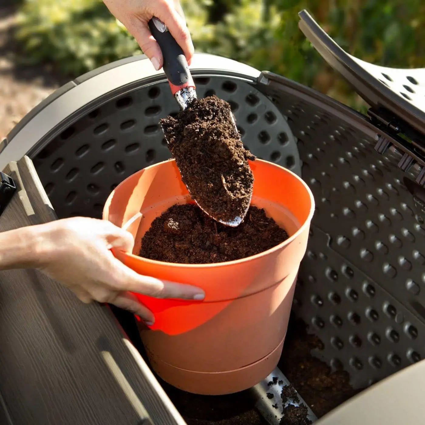 Terracotta pot with orange interior and black-handled trowel for gardening in a rotating composter