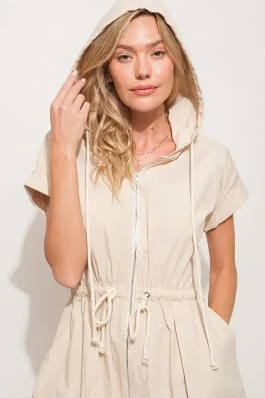 Blonde woman modeling beige hooded mini dress with short sleeves and string details