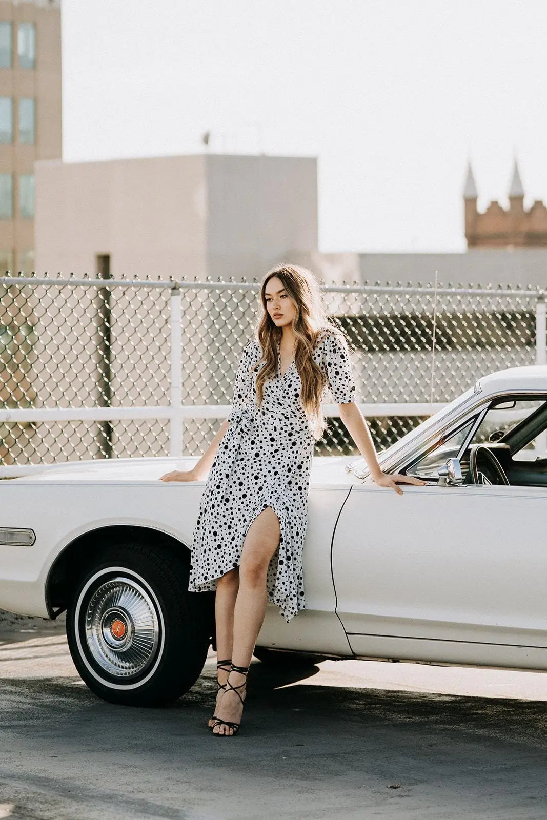 Woman in Coco Dress White polka dot with puffy sleeves and black lace-up heels beside vintage car