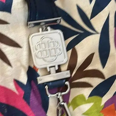 Silver-toned metal bag charm with embossed logo and navy leather strap for oversized floral canvas tote