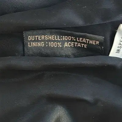 Black fabric label with white text showing material details on G III Black Leather Trench Coat