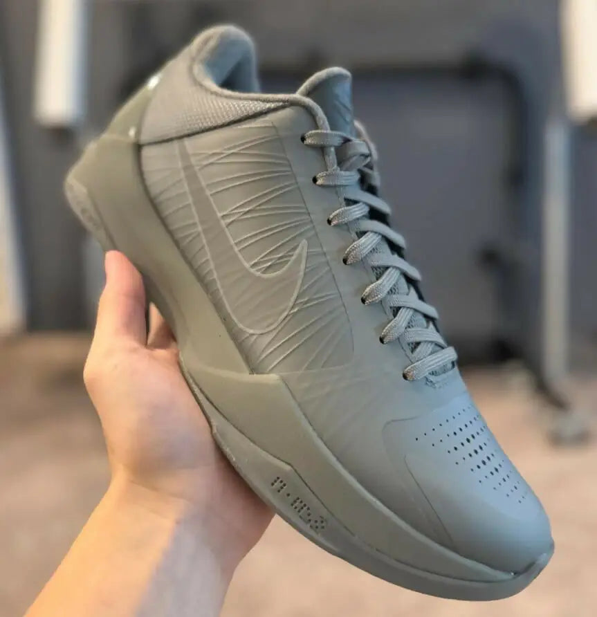 Hand holding Kobe 5 Fade To Black Nike basketball shoe with textured upper and swoosh