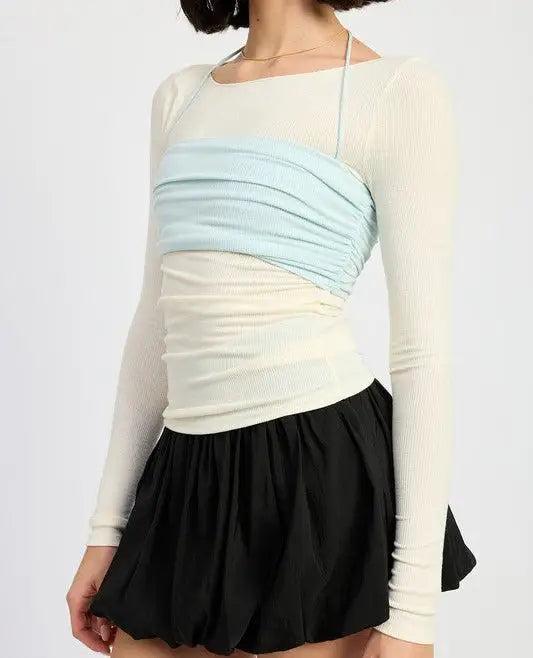 Woman wearing trendy long sleeve beige top with ruched long sleeve layered over blue bandeau and black mini skirt