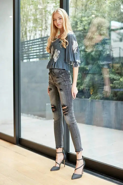 Woman wearing mid rise skinny jeans with ripped details, blue patterned top, and black heels