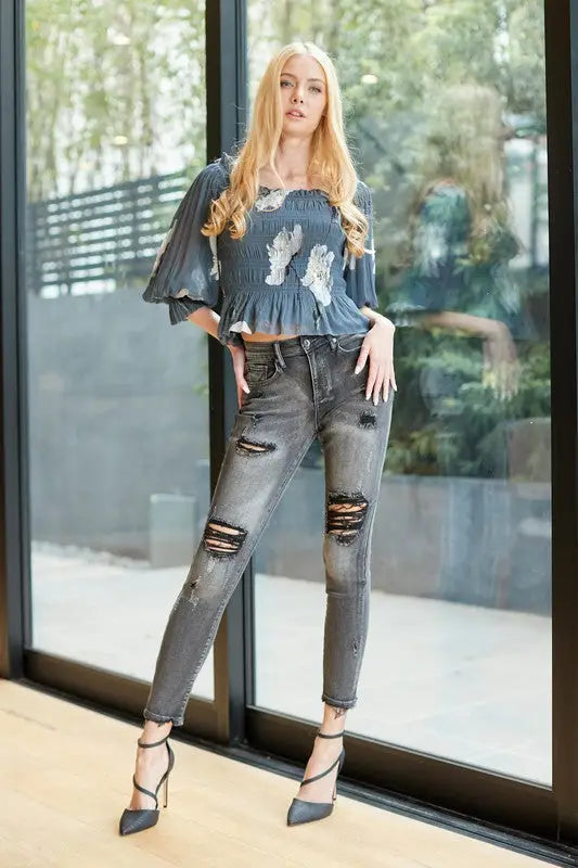 Woman wearing dark blue mid rise skinny jeans with white embroidery and ripped details