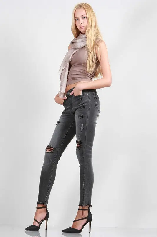 Young woman wearing mid rise skinny jeans with rips, light brown tank top, and black heels