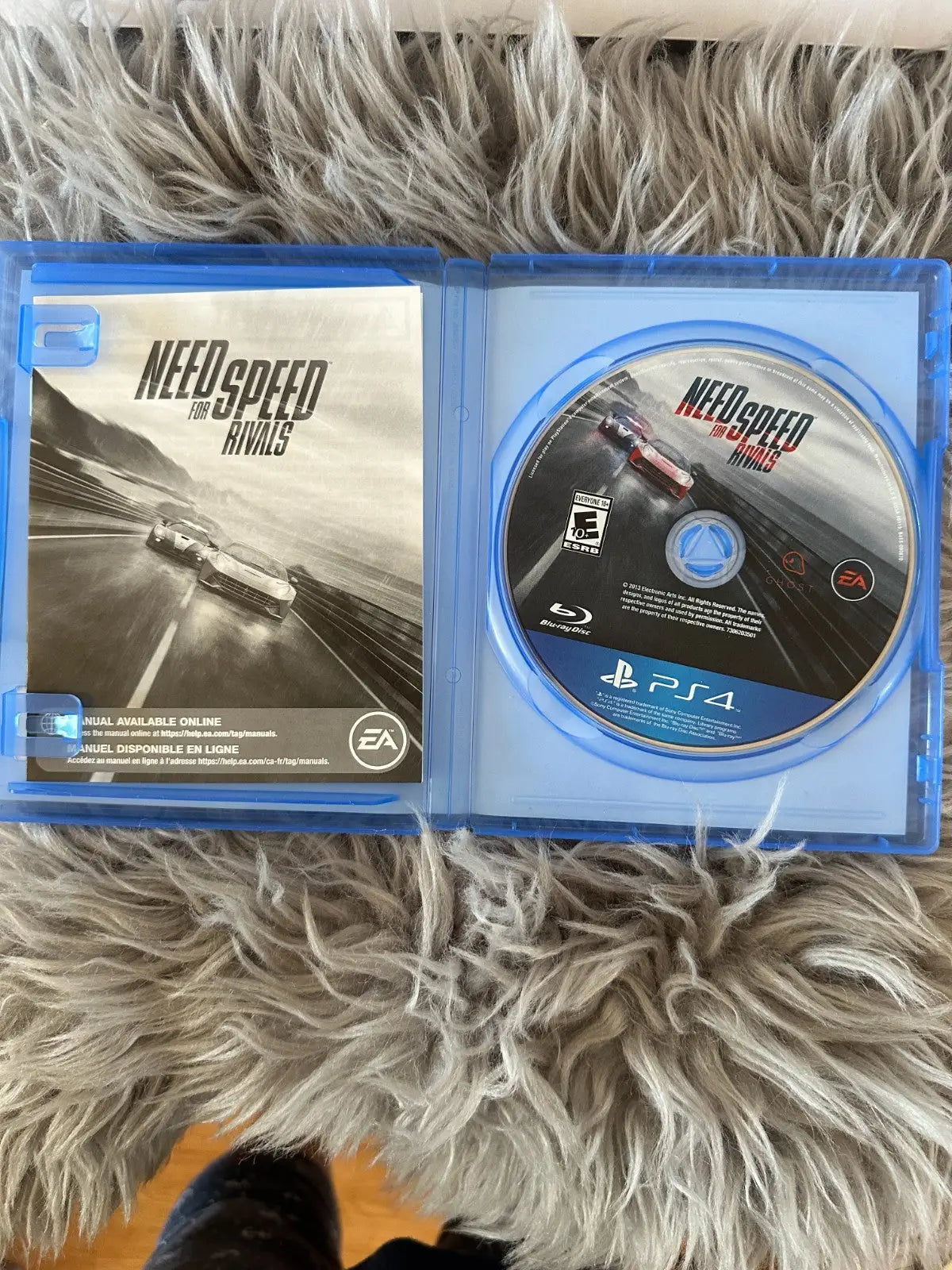 Open blue Sony PlayStation 4 case with Need for Speed Rivals racing action game disc and manual