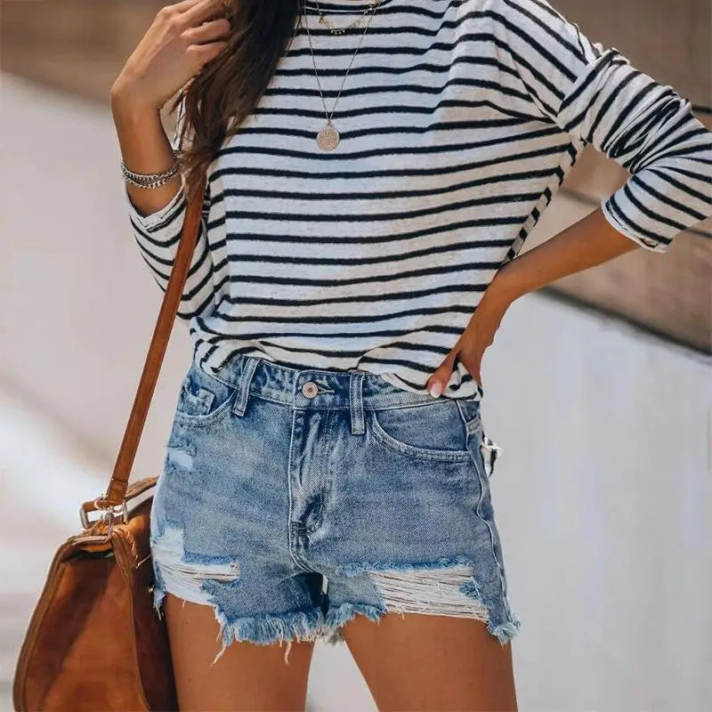Women fringe denim jeans shorts worn with a striped long-sleeve shirt and brown shoulder bag