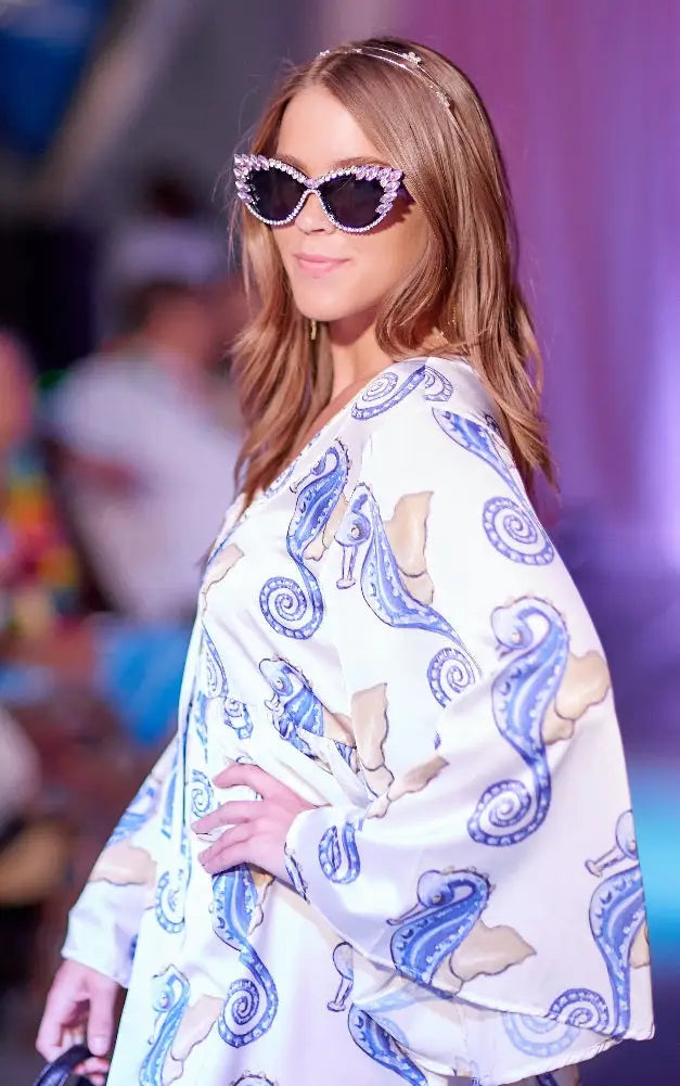 Woman in white mini dress with flare sleeves, blue seahorse pattern, cat-eye sunglasses
