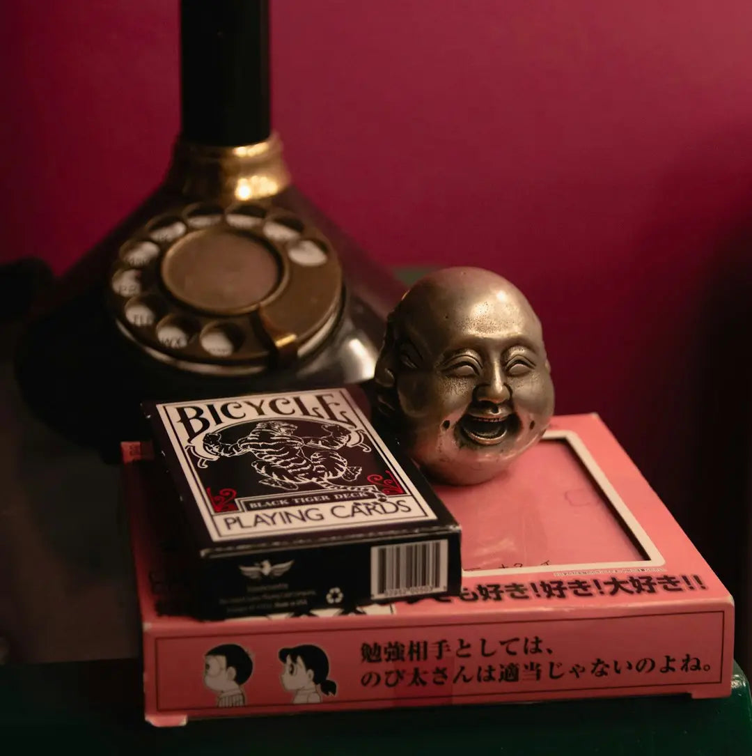 Smiling Buddha head statue alongside playing cards and a rotary telephone.