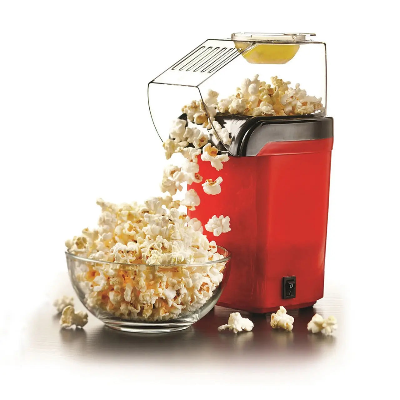 Red pop corn maker with clear plastic lid and handle, glass bowl filled with popcorn.