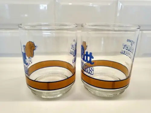 Two clear Pitt Panthers glasses with gold bands celebrating Big East basketball