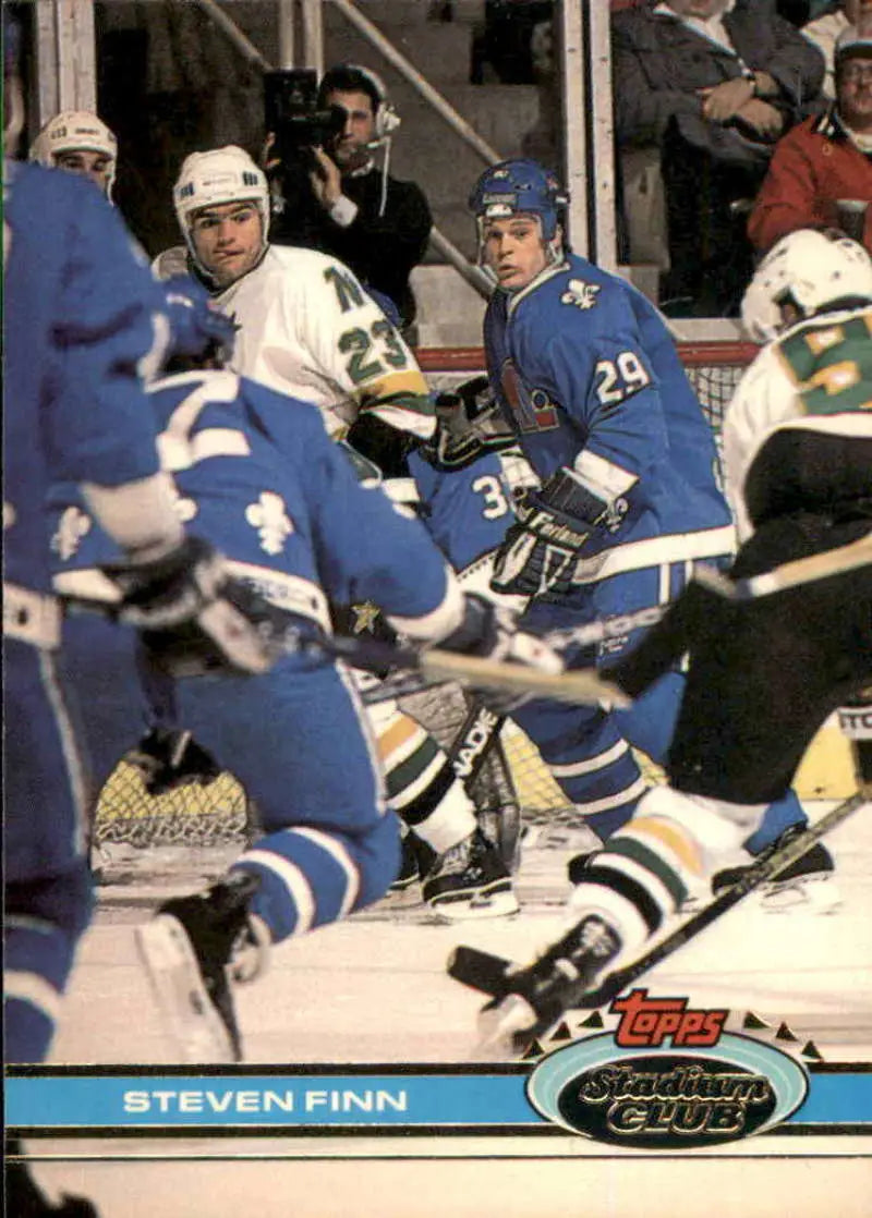 Hockey players in blue and white uniforms battle for the puck, featuring Steven Finn
