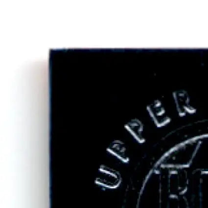 Black rectangular object with UPPER embossed, part of 1996 Upper Deck Racing Road to the Cup John Andretti #RC17a