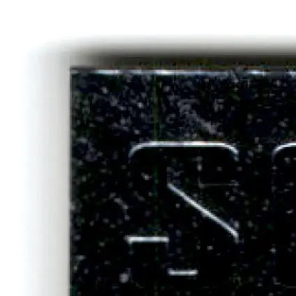 Dark speckled metal object with raised lettering from 1996 Upper Deck Racing Road to the Cup Rick Mast card