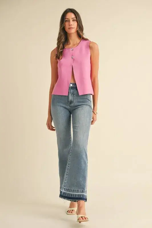 Women’s pink sleeveless crop sweater vest with metal button detail and distressed flare jeans