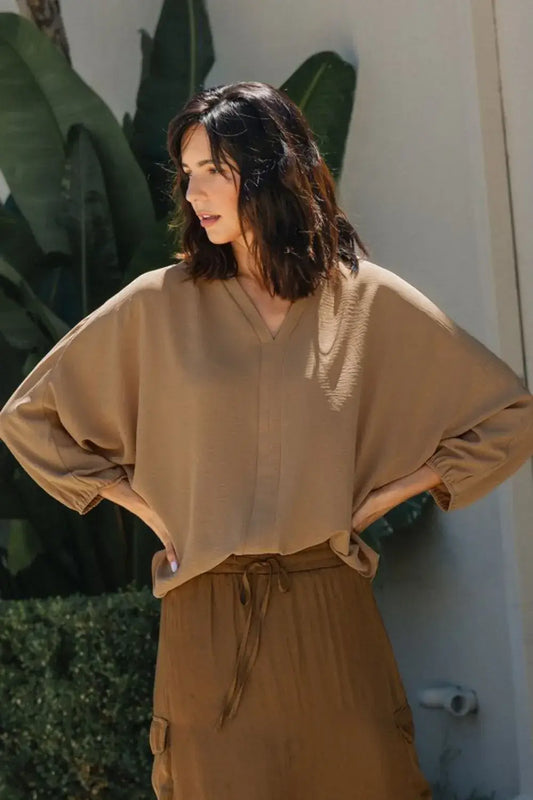 Beige oversized v-neck sweater with drawstring waist and pocket detail, featuring notched batwing sleeve design
