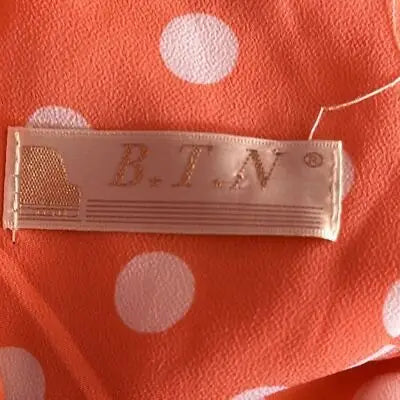 Beige clothing label with B.T.N. logo and grand piano, featuring dress white polka dots