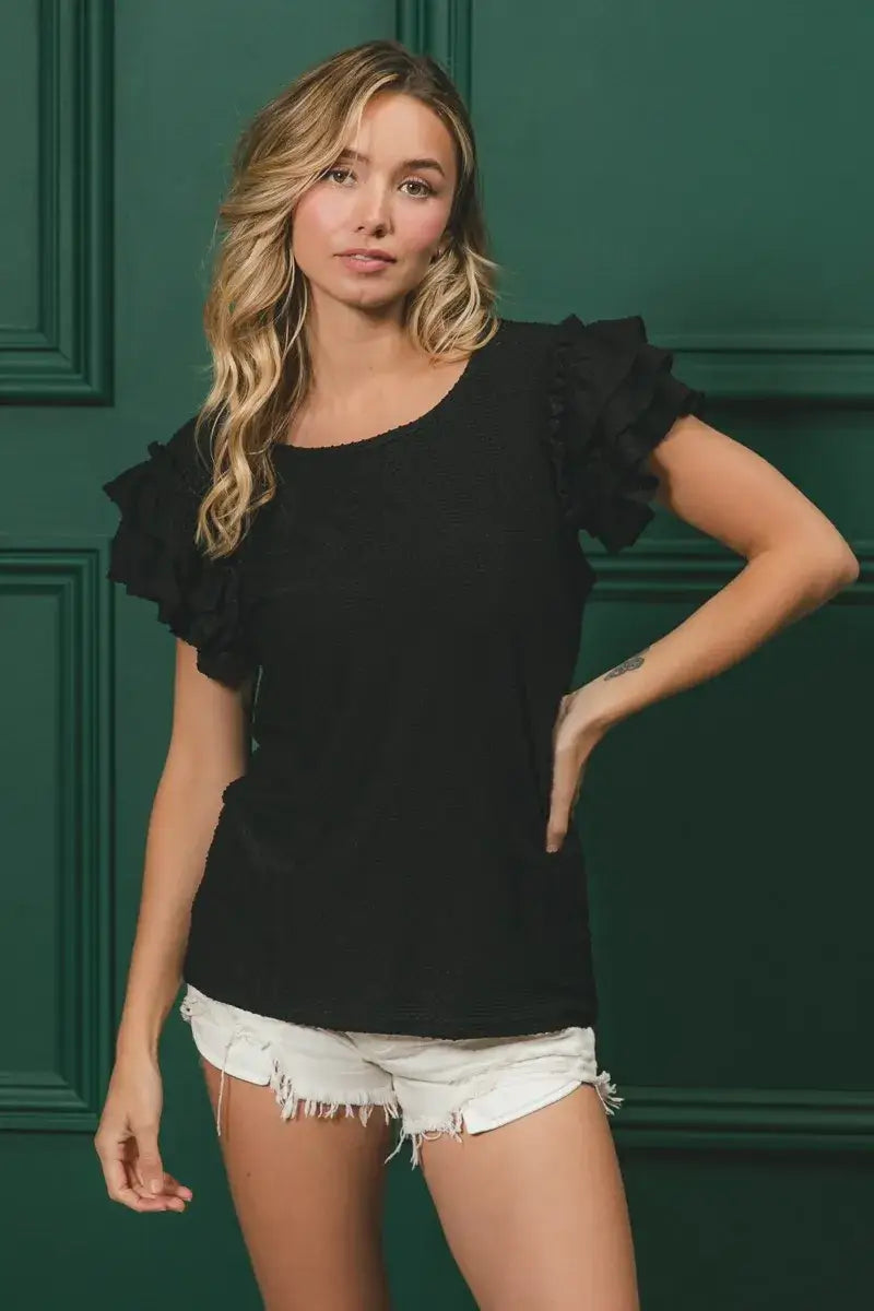 Black ruffled sleeve top with birdseye texture layered design and frayed denim shorts
