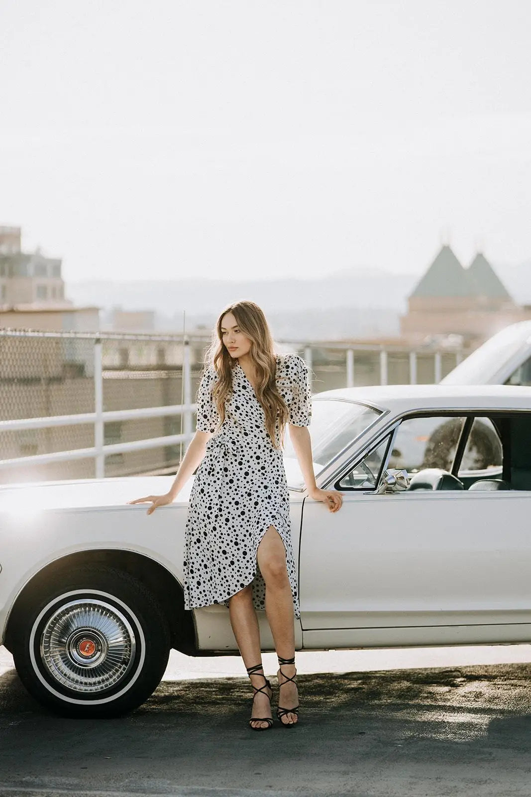 Woman in Coco Dress White polka dot with puffed sleeves and black heels next to vintage car