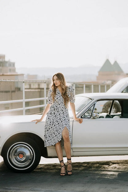 Woman in Coco Dress White polka dot with puffed sleeves and black heels next to vintage car