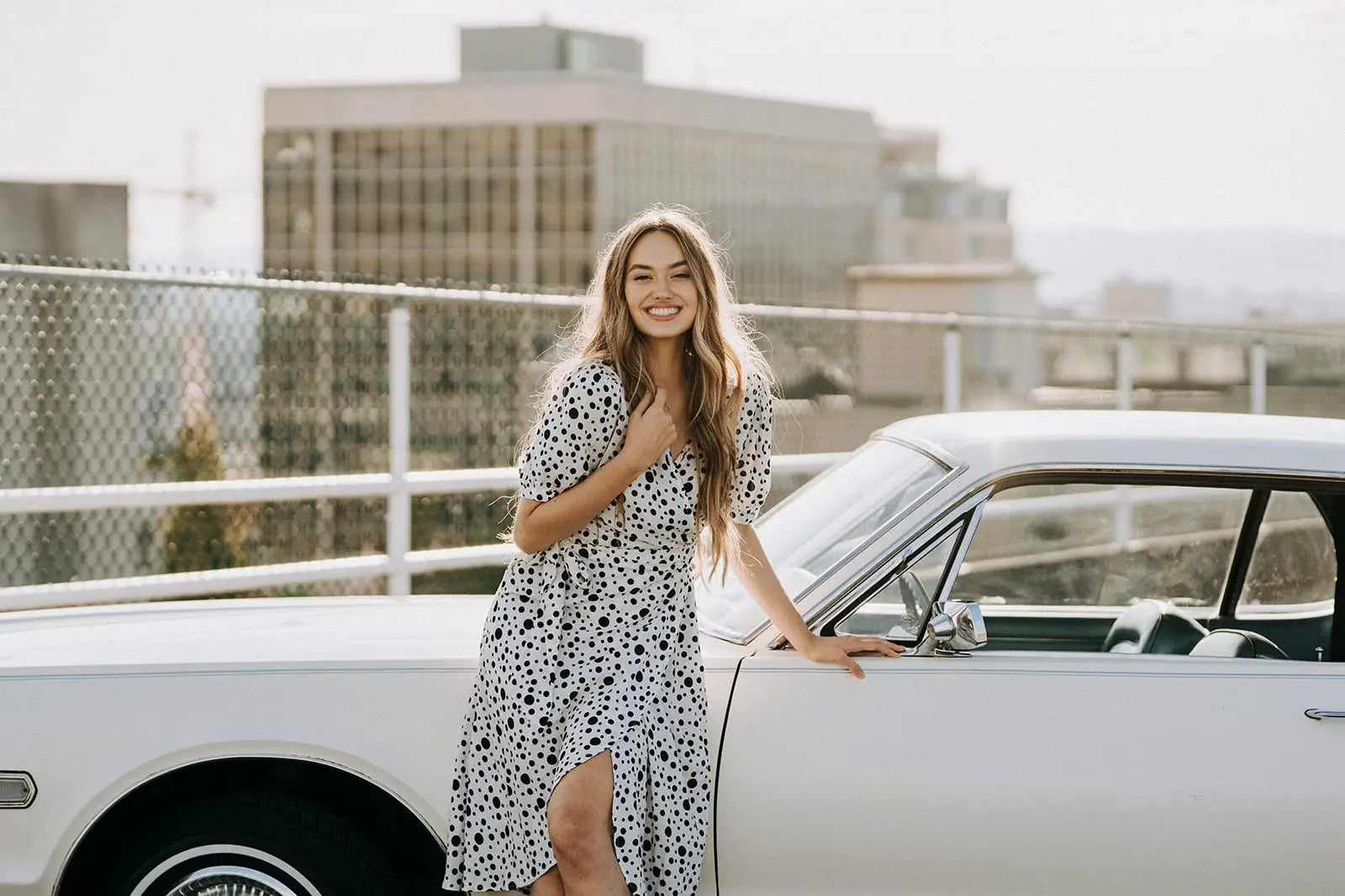 Smiling woman in Coco Dress White Polka Dot leaning on vintage car, perfect for business days