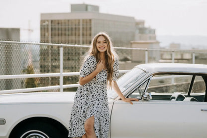 Smiling woman in Coco Dress White Polka Dot leaning on vintage car, perfect for business days