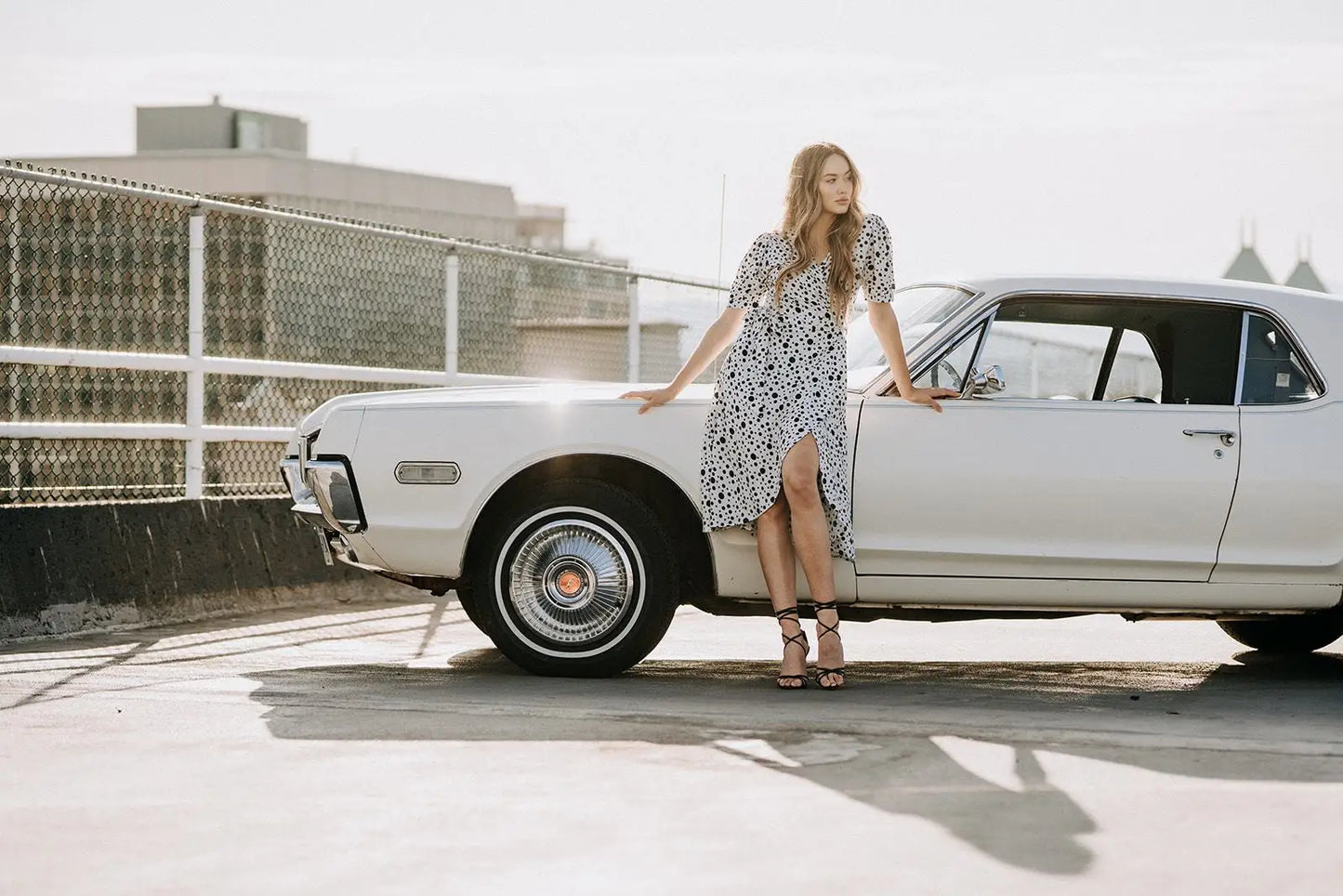 Woman in Coco Dress White Polka Dot with high heels leaning on vintage white car