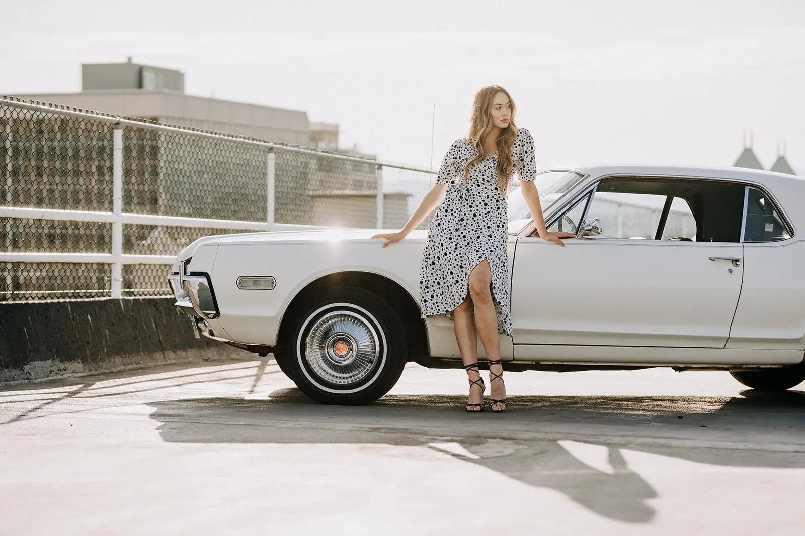 Woman in Coco Dress White Polka Dot with high heels leaning on vintage white car