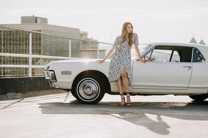 Woman in Coco Dress White Polka Dot with high heels leaning on vintage white car