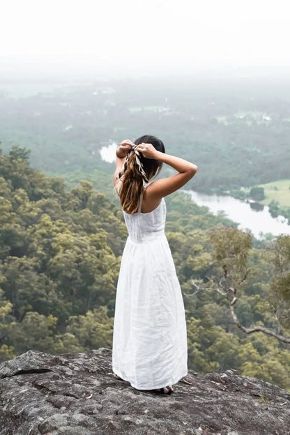 Woman in a white linen dress tying her hair, showcasing the Daria Linen Dress