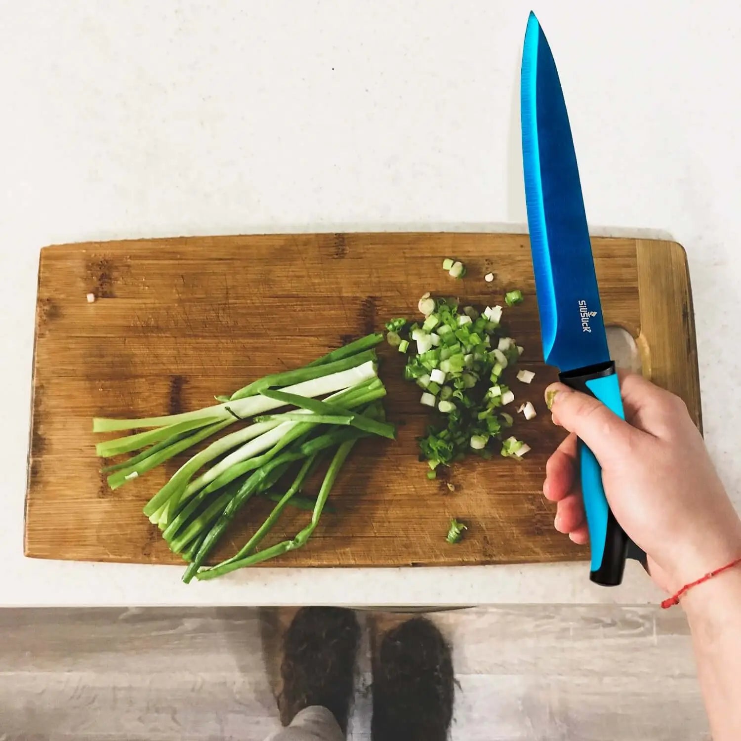 Blue kitchen knife from knife set kit used to chop green onions on wooden board