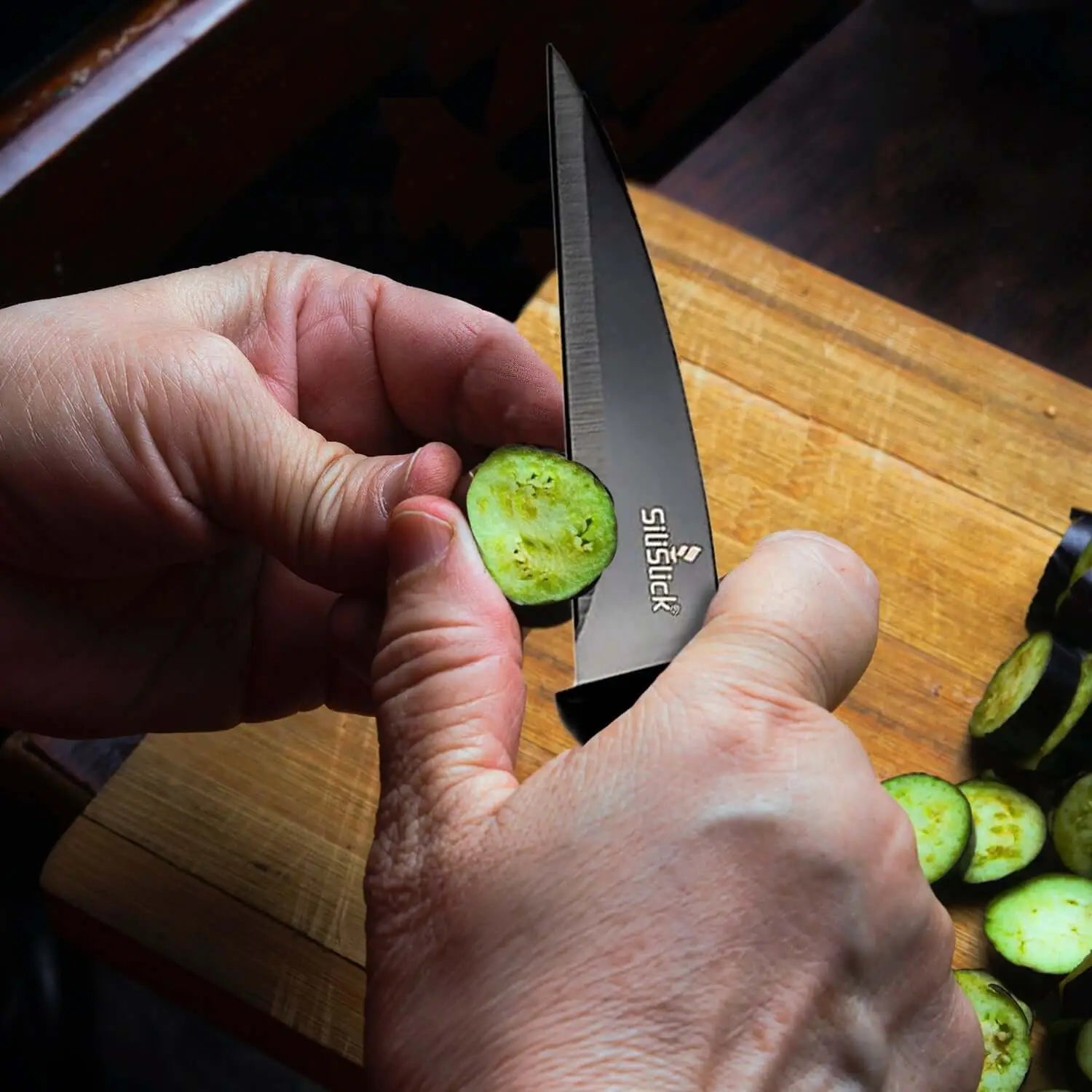 Hand holding black kitchen knife from knife set kit slicing fresh green vegetable