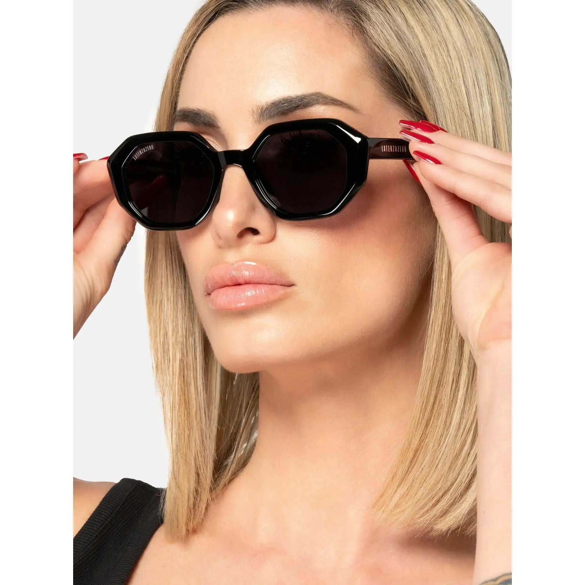 Woman wearing black hexagonal cat-eye UV3 Veritas_X242 sunglasses with dark lenses