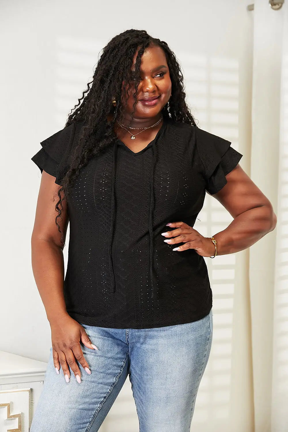 Black eyelet flutter sleeve blouse with layered necklaces and tie-neck design