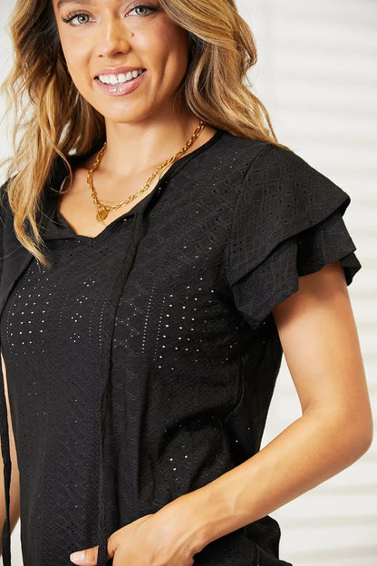 Black flutter sleeve blouse with eyelet tie-neck, gold necklace, and bracelet