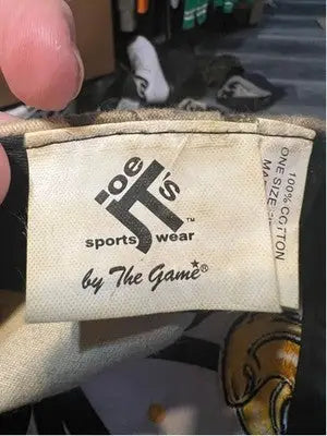 White clothing tag with black text attached to Men’s The Game USM Golden Eagles Camo Yellow Baseball Cap