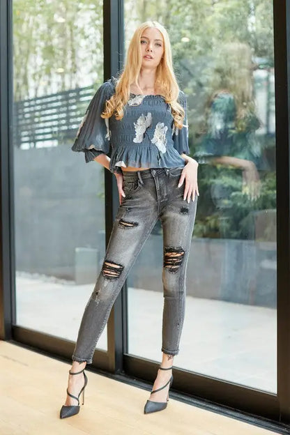 Woman wearing dark blue mid rise skinny jeans with white embroidery and ripped details