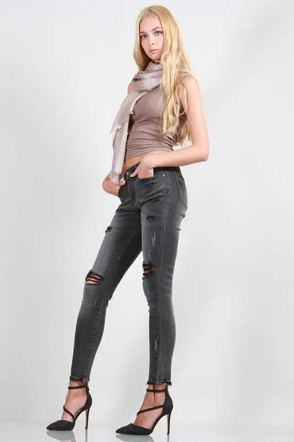 Young woman wearing mid rise skinny jeans with rips, light brown tank top, and black heels