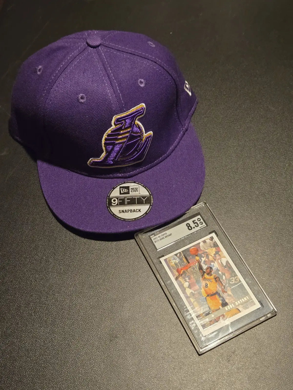 Purple Los Angeles Lakers baseball cap and graded Kobe Bryant card in product listing