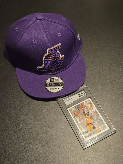 Purple Los Angeles Lakers baseball cap and graded Kobe Bryant card in product listing