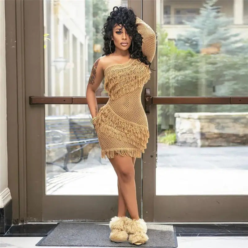 Woman in beige inclined shoulder knit mini dress with fringe and fluffy boots