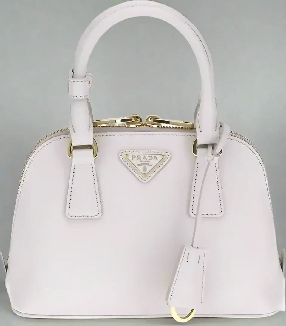 Light pink leather handbag with gold hardware, zip closure, and logo patch by PRADA