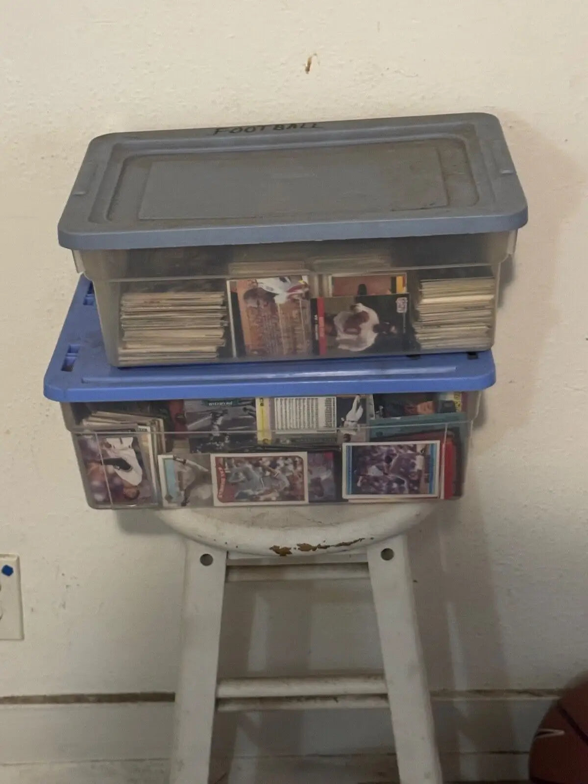 Two stacked plastic storage containers filled with trading cards on a white stool