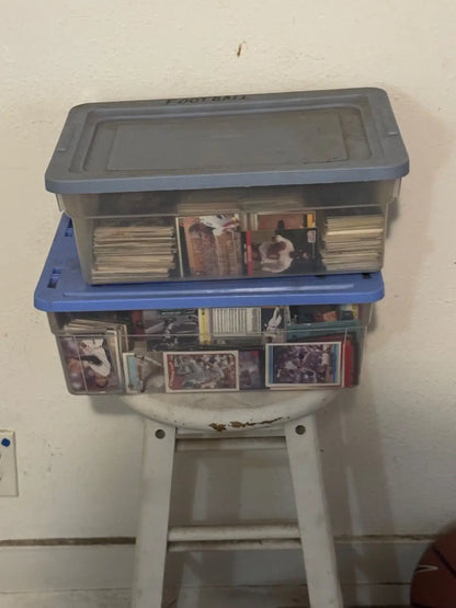 Two stacked plastic storage containers filled with trading cards on a white stool