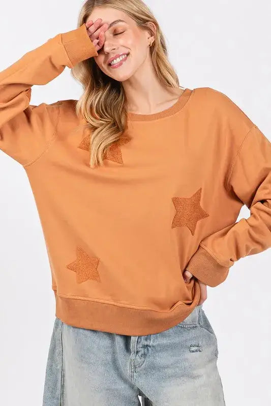 Rust-colored SAGE + FIG star patch long sleeve sweatshirt with distressed denim jeans