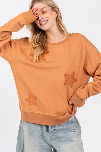 Rust-colored SAGE + FIG star patch long sleeve sweatshirt with distressed denim jeans
