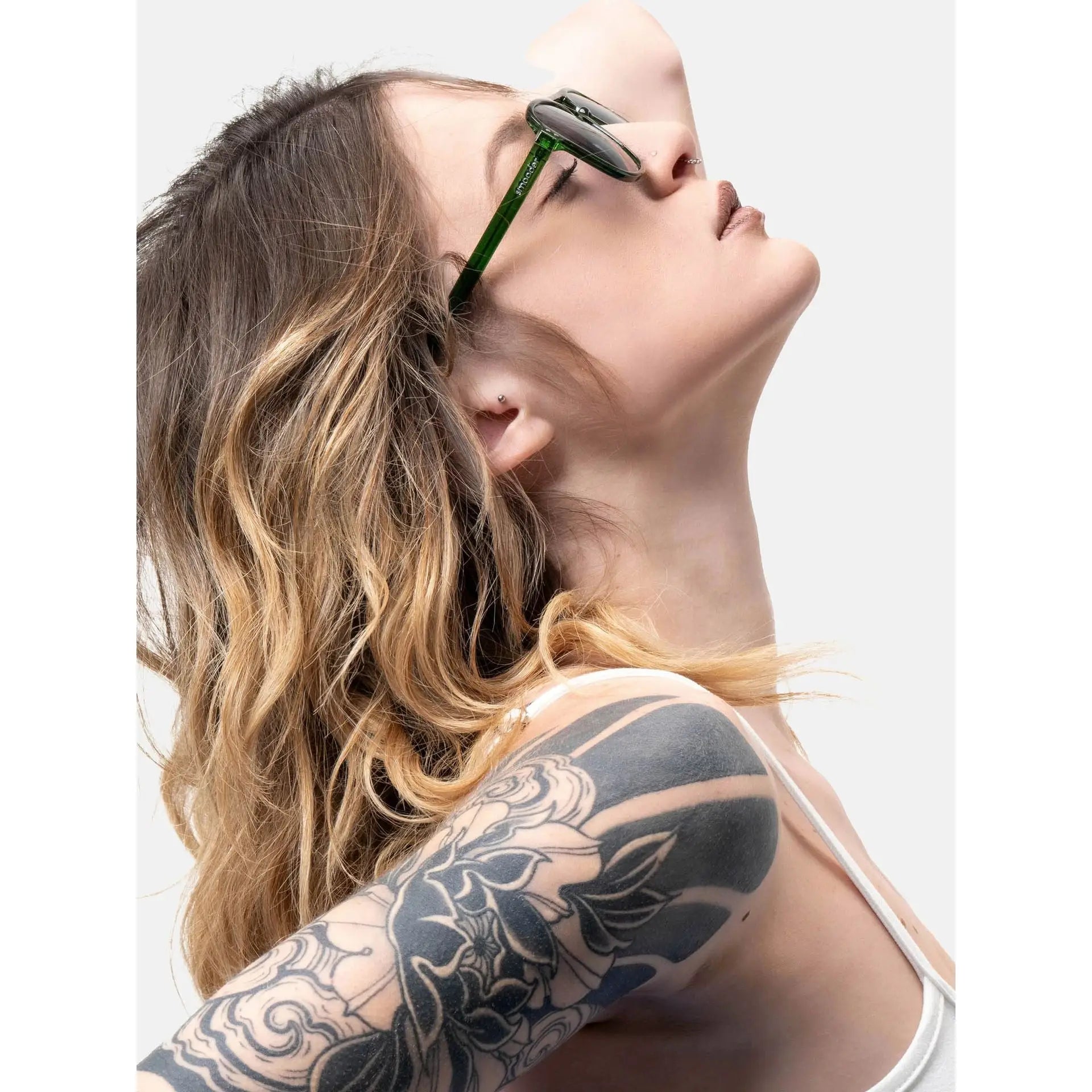 Woman with wavy blonde hair wearing Smooder sunglasses and a tattoo sleeve