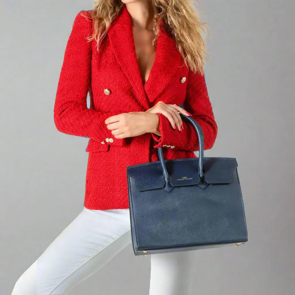 Woman wearing red tweed blazer with gold buttons and holding a navy synthetic leather tote bag